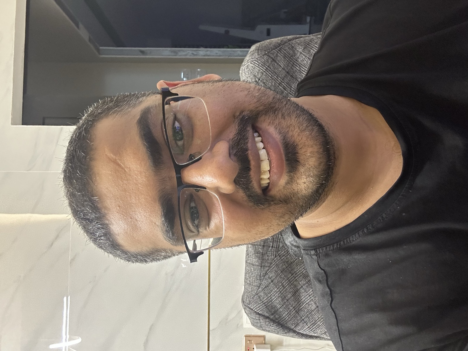 Omer smiling at Klinik Muhibbah — glasses reflecting clinic lights