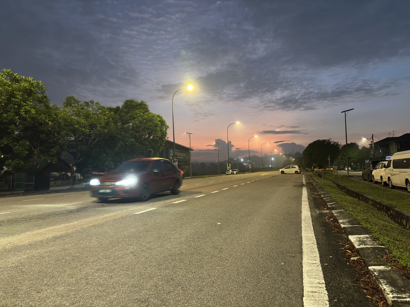 Car passing at dawn — red taillights blurring in pink light on wet asphalt