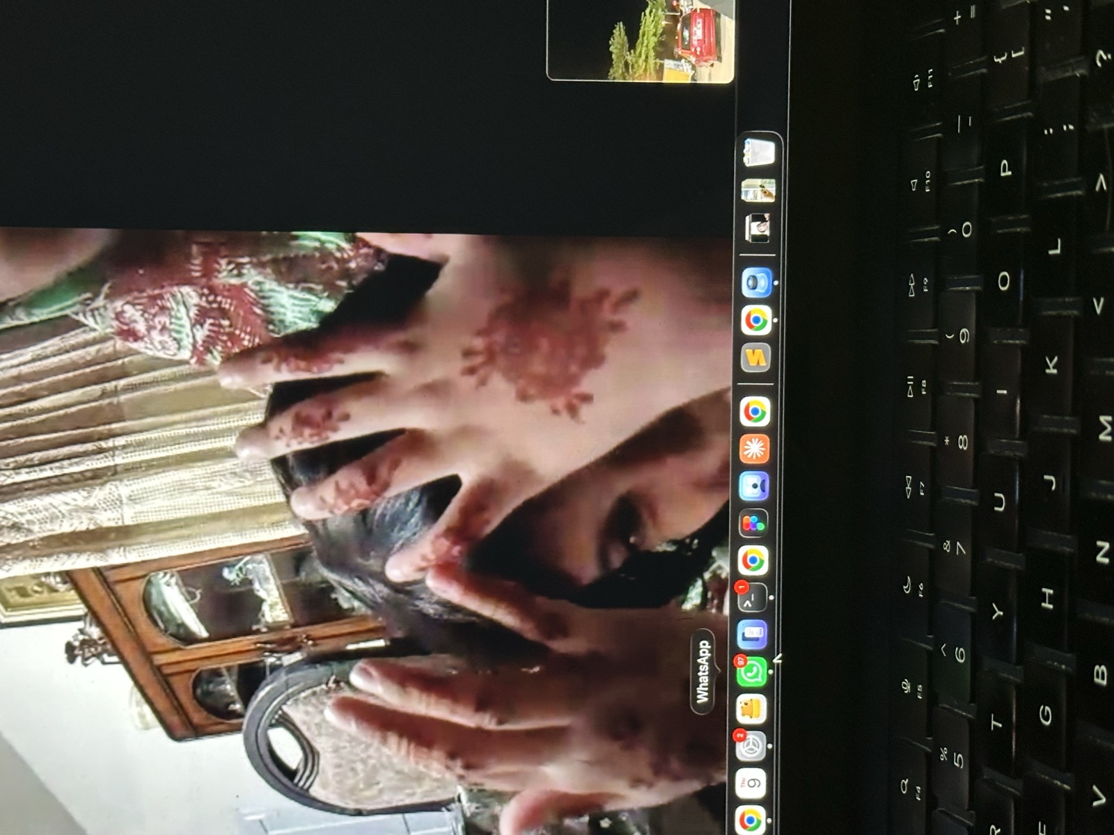 Video call on MacBook — henna-decorated hands held up to camera, family in Pakistan