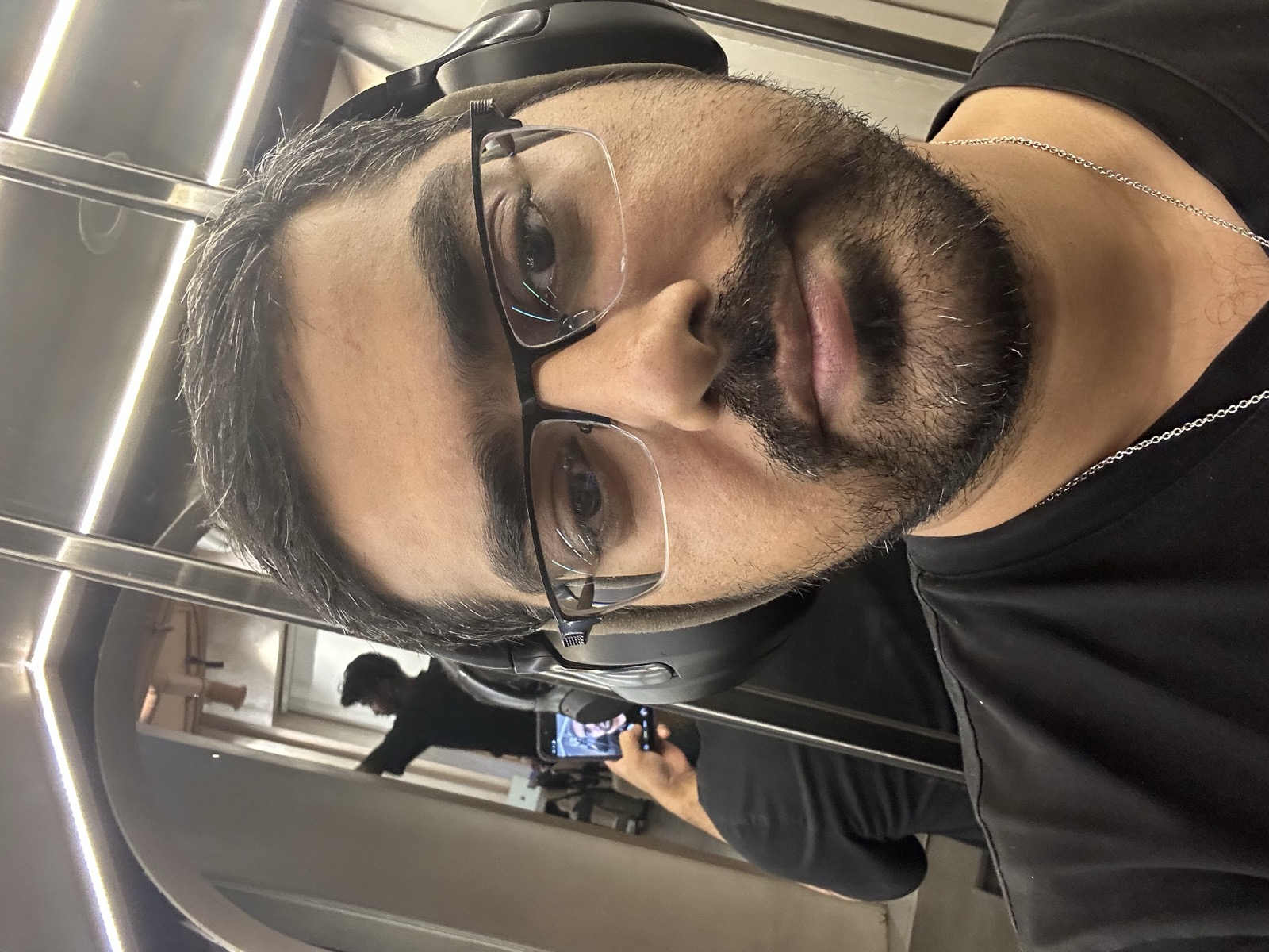 Admin close-up elevator portrait — rectangular glasses, beard, silver chain, black t-shirt — 3:05 AM May 10, 2026 — clearest portrait of the trip