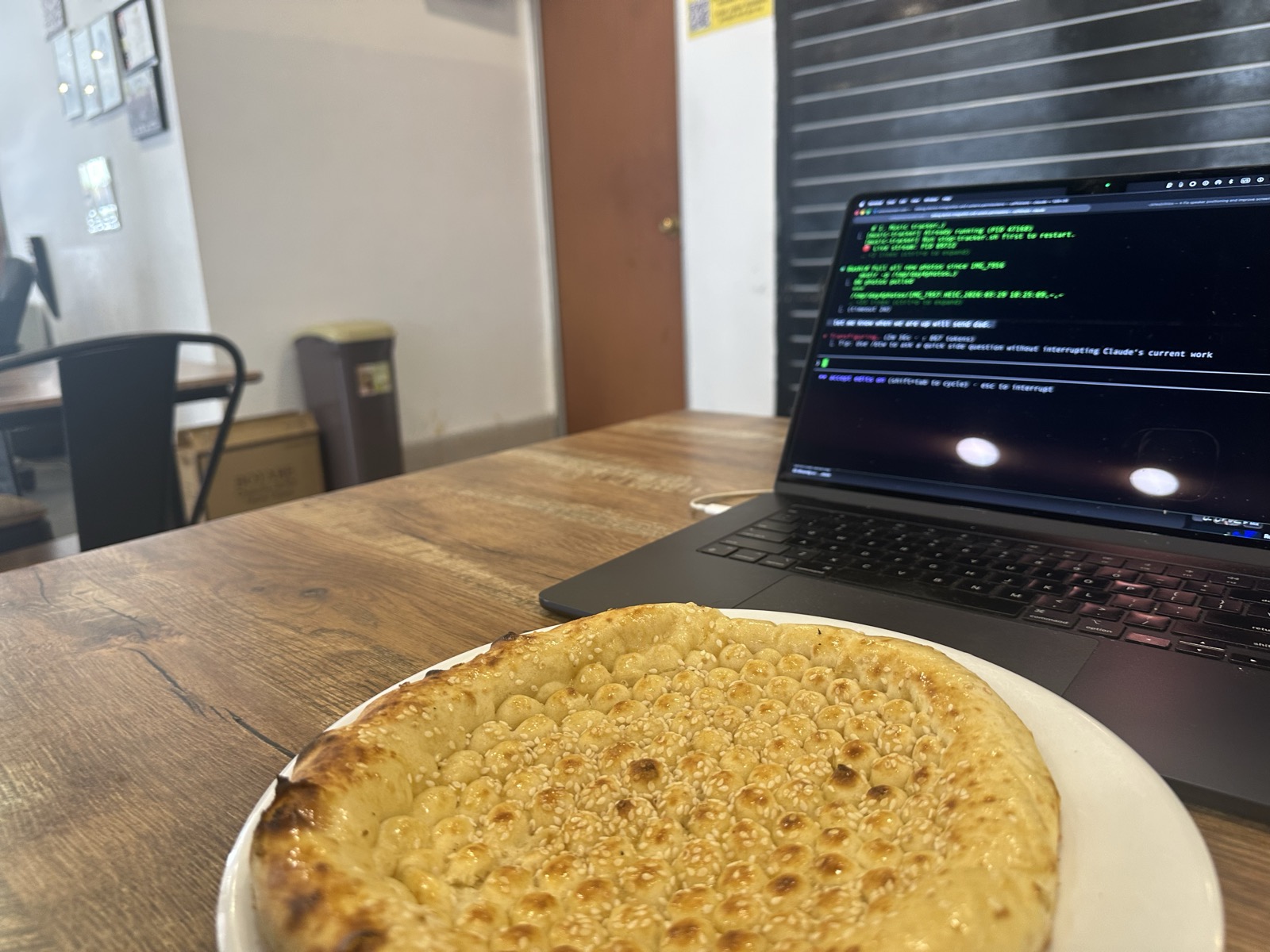 Afghan taboon bread on white plate, MacBook with Claude Code terminal running — KL evening, Day 4
