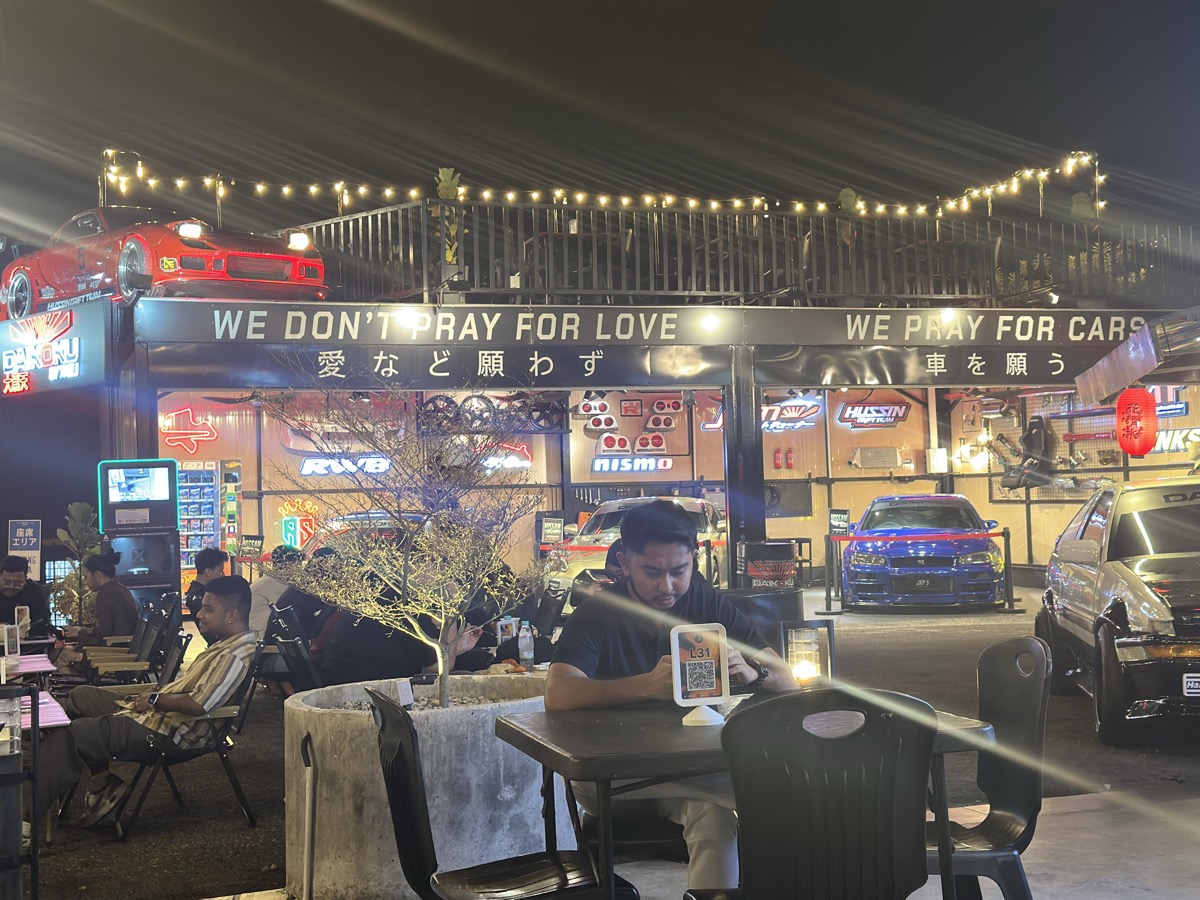 Car cafe in Johor Bahru at night — WE DON'T PRAY FOR LOVE, WE PRAY FOR CARS sign