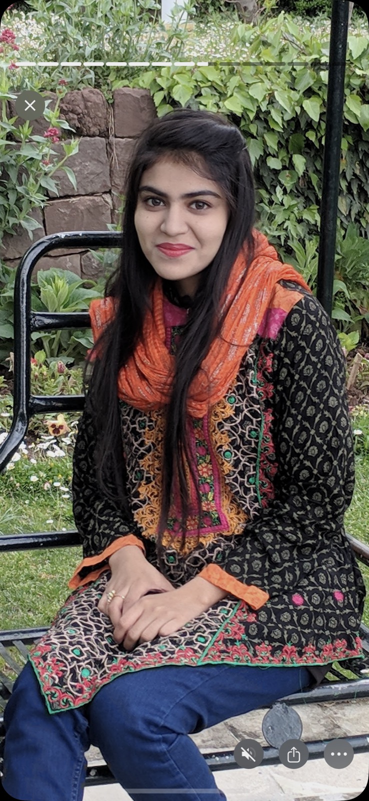 Maria sitting on a bench — black kameez, orange scarf, smiling