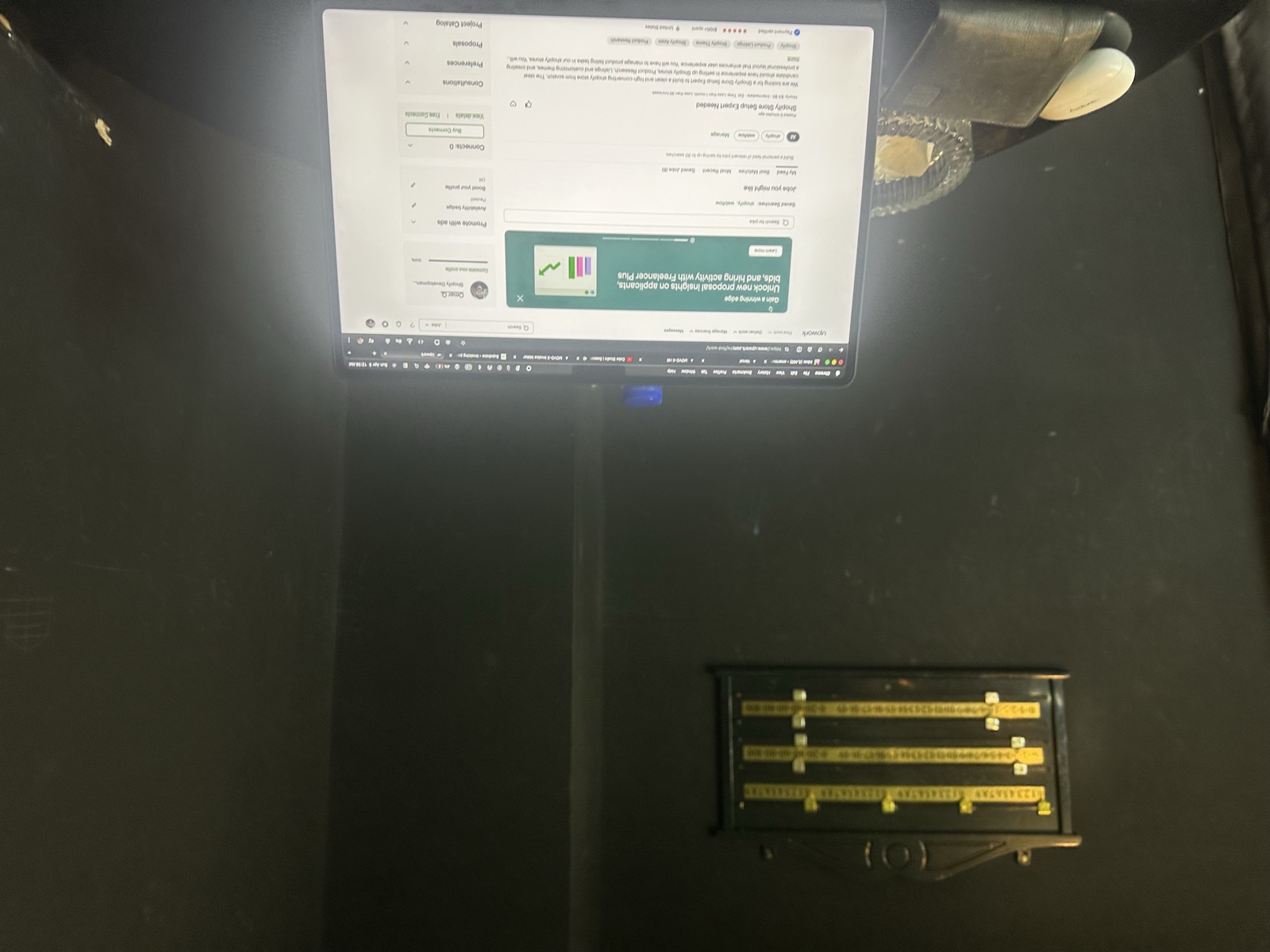 MacBook glowing in dark hotel room — Budget Online Shopify dashboard, cash register beside it